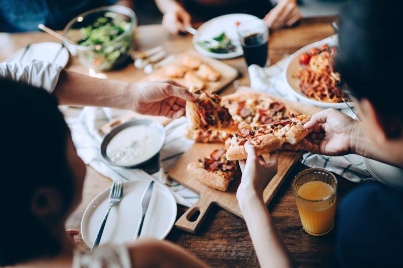 Close up of a young group of friends passing and serving food while enjoying together. They are having fun, chatting and feasting on food and drinks at dinner party