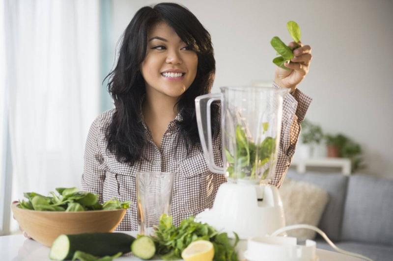 A woman makes a green smoothie in a blender.