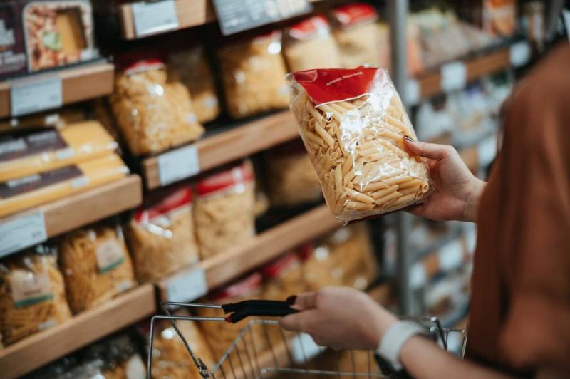 Young Asian woman carrying a shopping basket, grocery shopping in supermarket, close up of her hand choosing a pack of organic pasta along the aisle. Healthy eating lifestyle