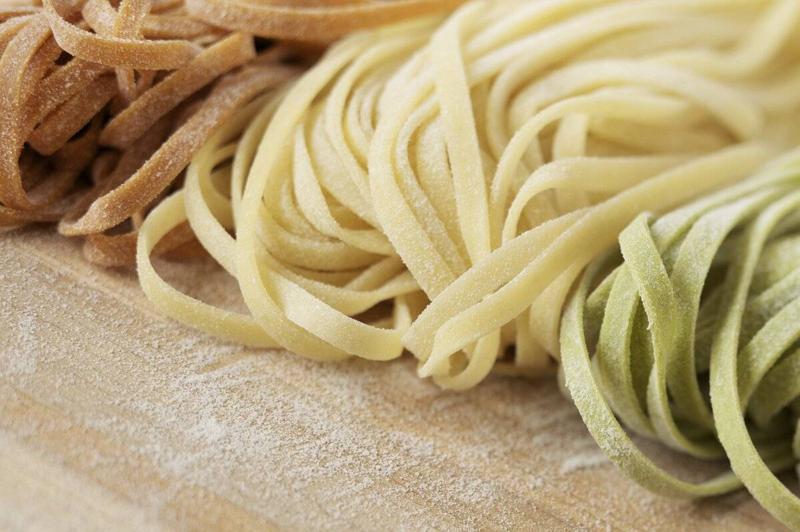 Natural light image of fresh tri-colored linguine pasta on wood. The three colors represent the colors in the Italian flag.